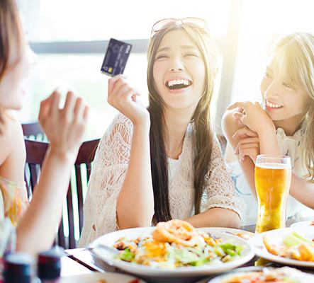 girls laughing at meal while one holds card to pay