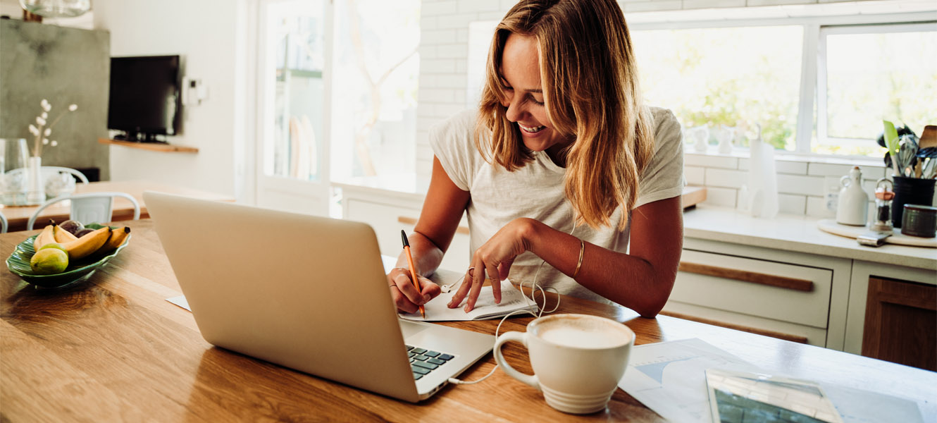 Woman looking at laptop writing something down.