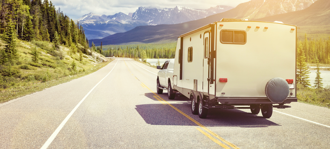 A truck driving down a scenic highway with a 5th wheel trailer in tow.