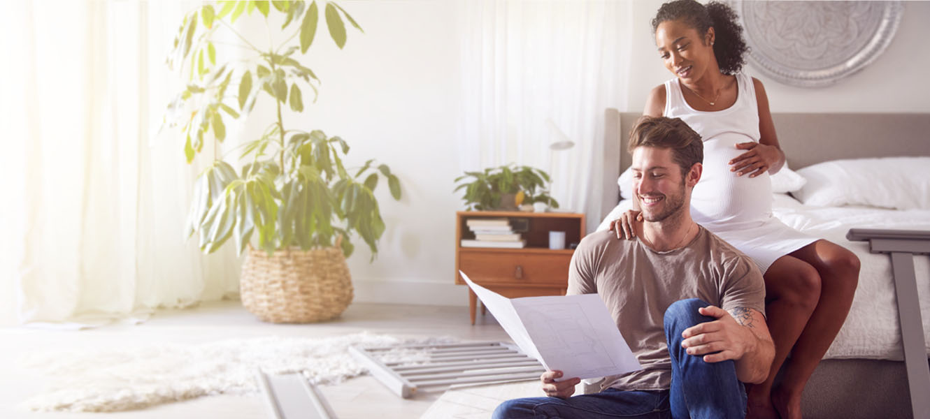 Couple sitting at the edge of the bed, woman is pregnant.