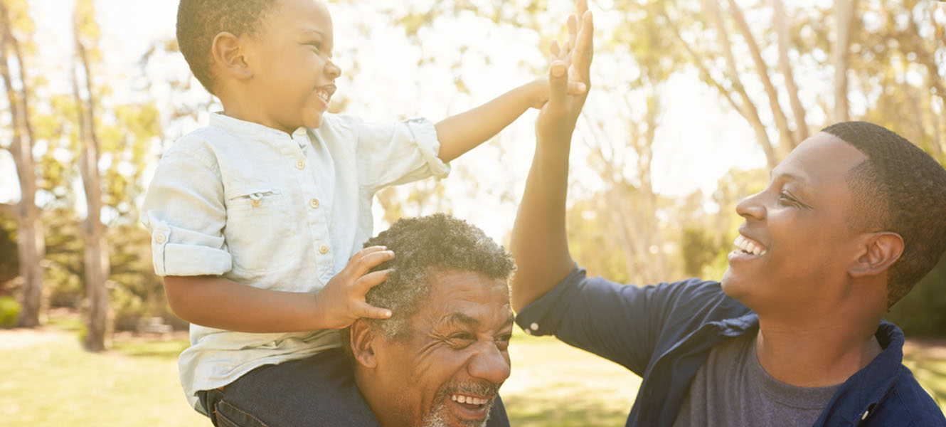 Grandpa with grandson on shoulders, high fiving dad.